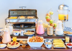 A buffet with various breakfast items including waffles, fruit, and beverages.