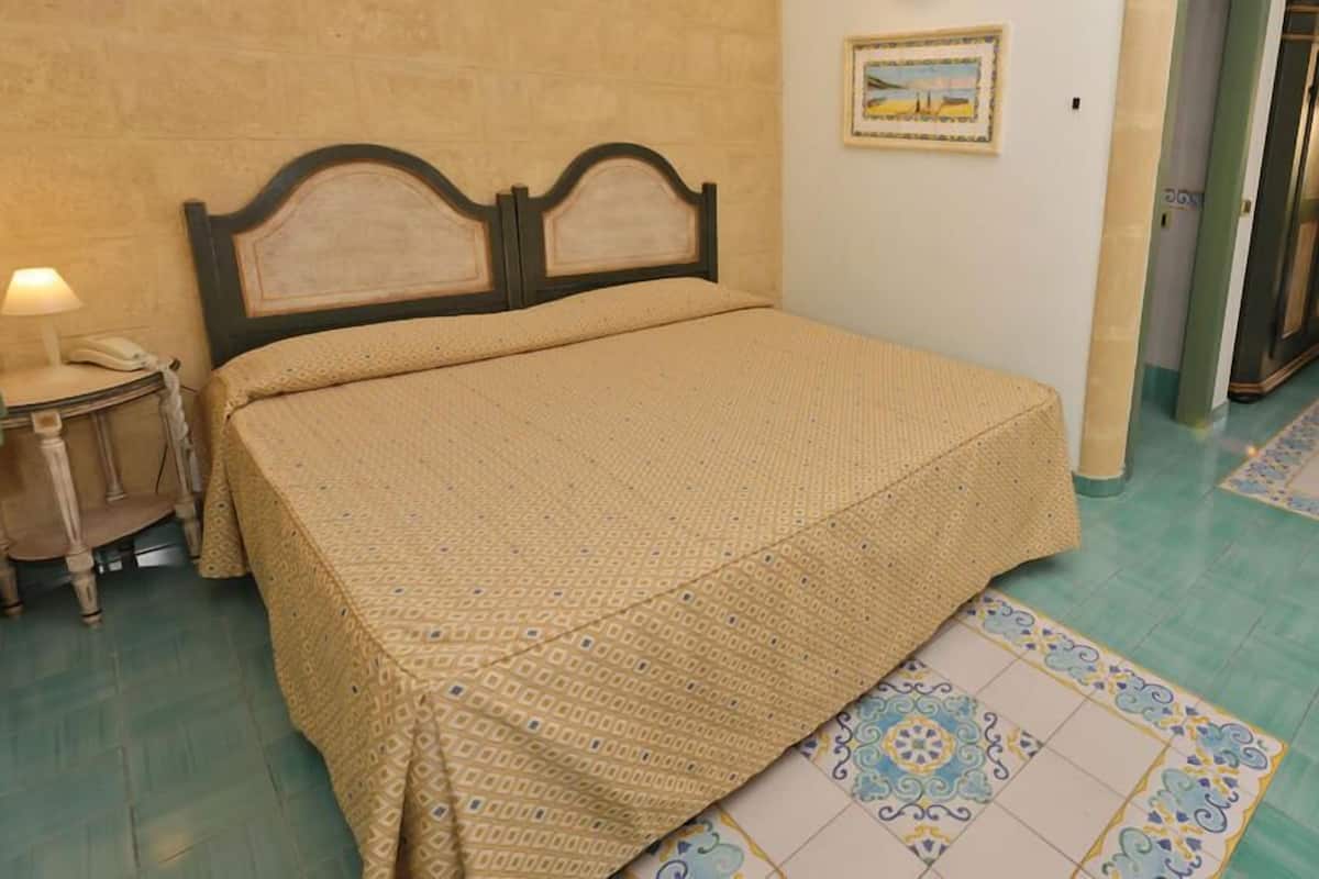 A bed with a patterned bedspread, a bedside table with a lamp, and a wall-mounted painting.