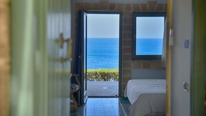 Une chambre avec un lit, une fenêtre donnant sur la mer et une porte menant à une autre pièce.