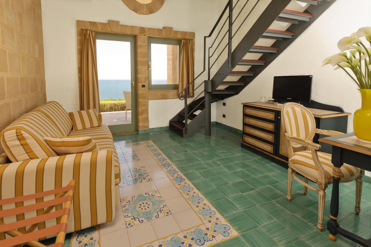 A living room with a sofa, a chair, a desk with a computer, a TV, and a staircase.