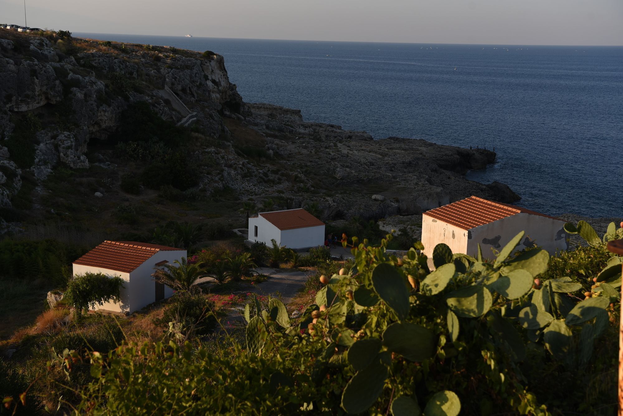 A coastal property with three white buildings, rocky cliffs, and a view of the sea.