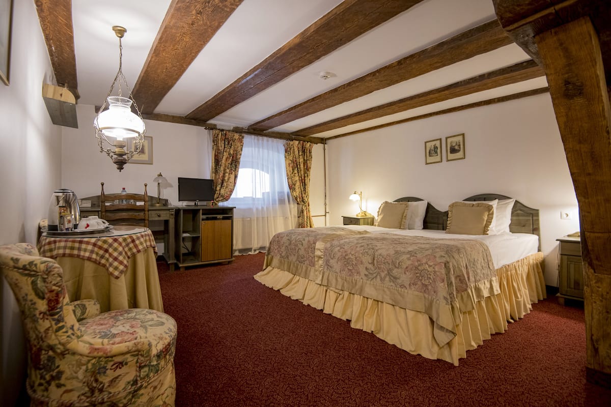 A hotel room with a large bed, a desk with a computer, a chair, and a table with a lamp.