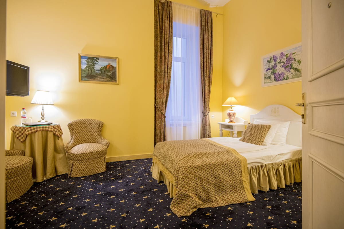A hotel room with a bed, a chair, a table with a lamp, and a painting on the wall.