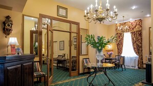 A hotel room with a green carpet, wooden furniture, a chandelier, and a large mirror. - Gutenbergs Hotel (Riga)