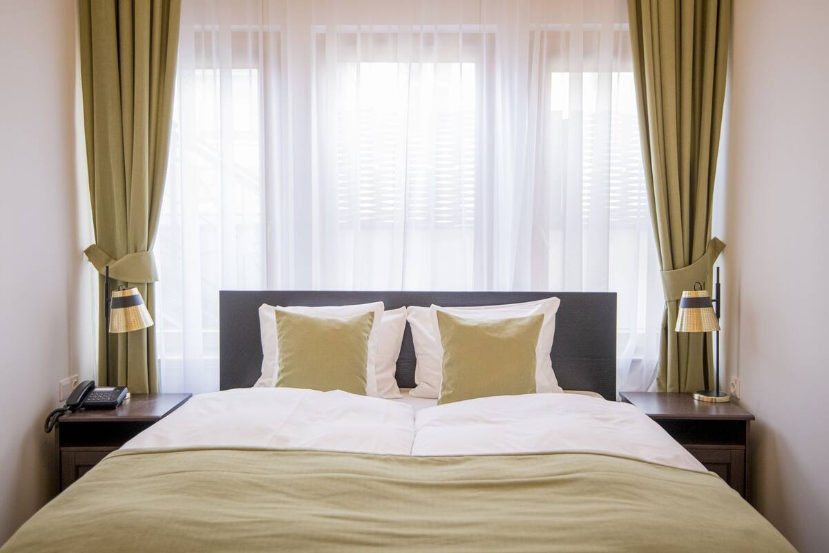 A neatly made bed with two pillows, a bedside lamp, and a phone on a nightstand.