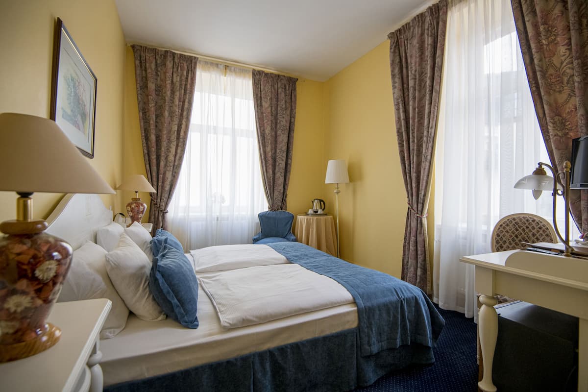 A hotel room with two beds, a desk, a chair, a lamp, a vase, and curtains.