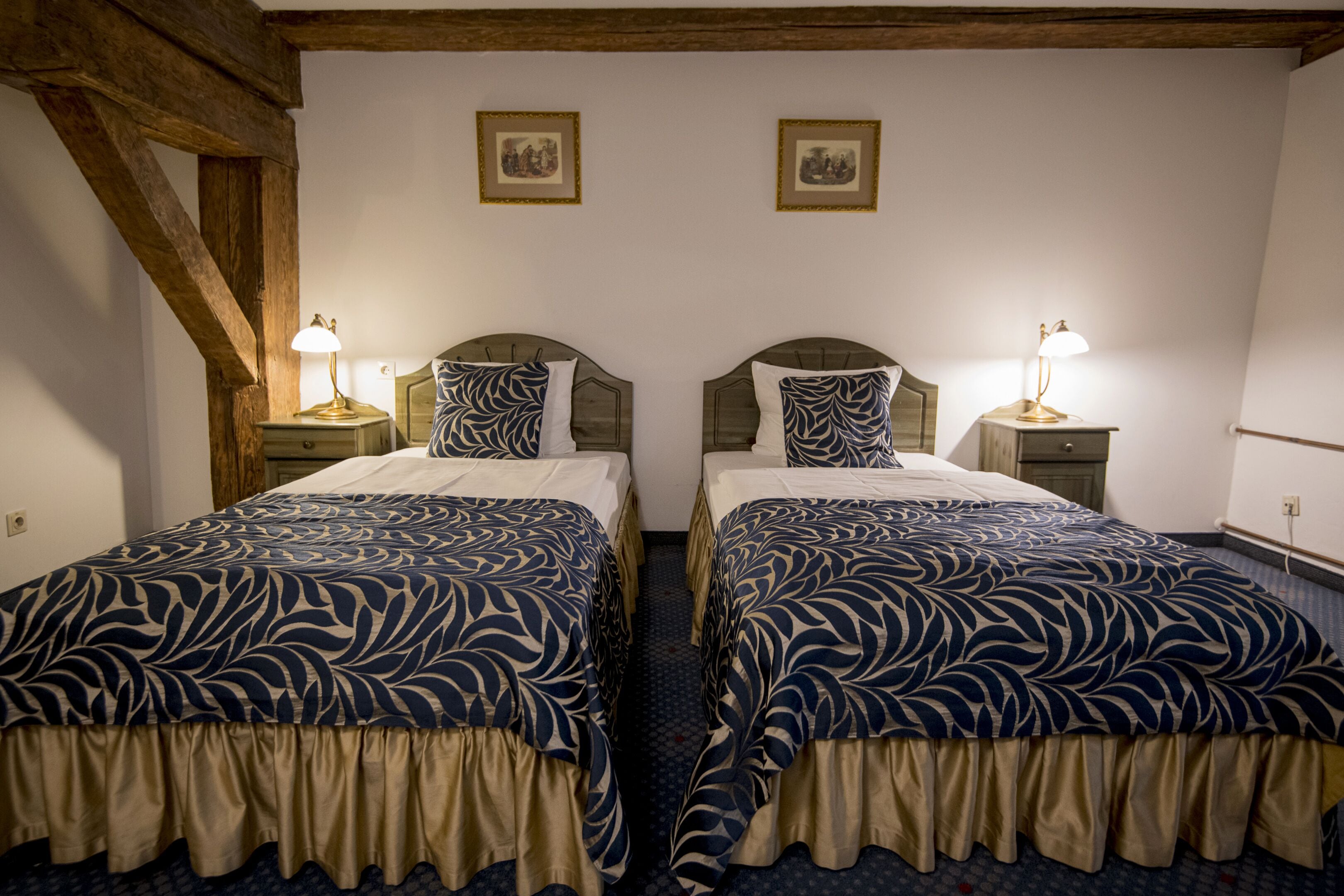 A hotel room with two single beds, each with a matching headboard and bedside table. The room has a wooden ceiling and a simple, clean design.