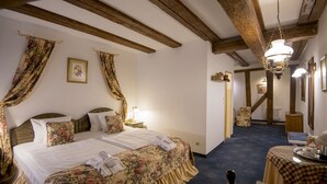 A hotel room with a bed, a nightstand, a table with a checkered tablecloth, and a chandelier. - Gutenbergs Hotel (Riga)