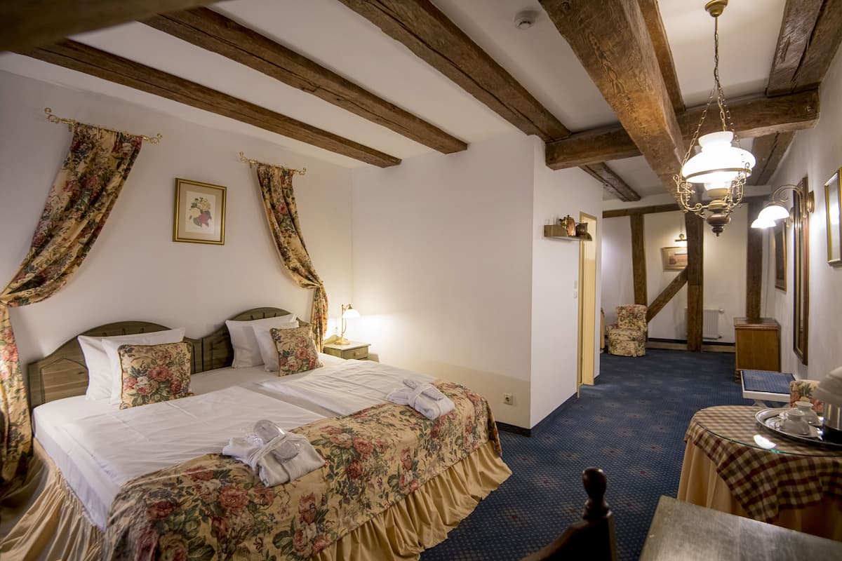 A hotel room with a bed, a nightstand, a table with a checkered tablecloth, and a chandelier.