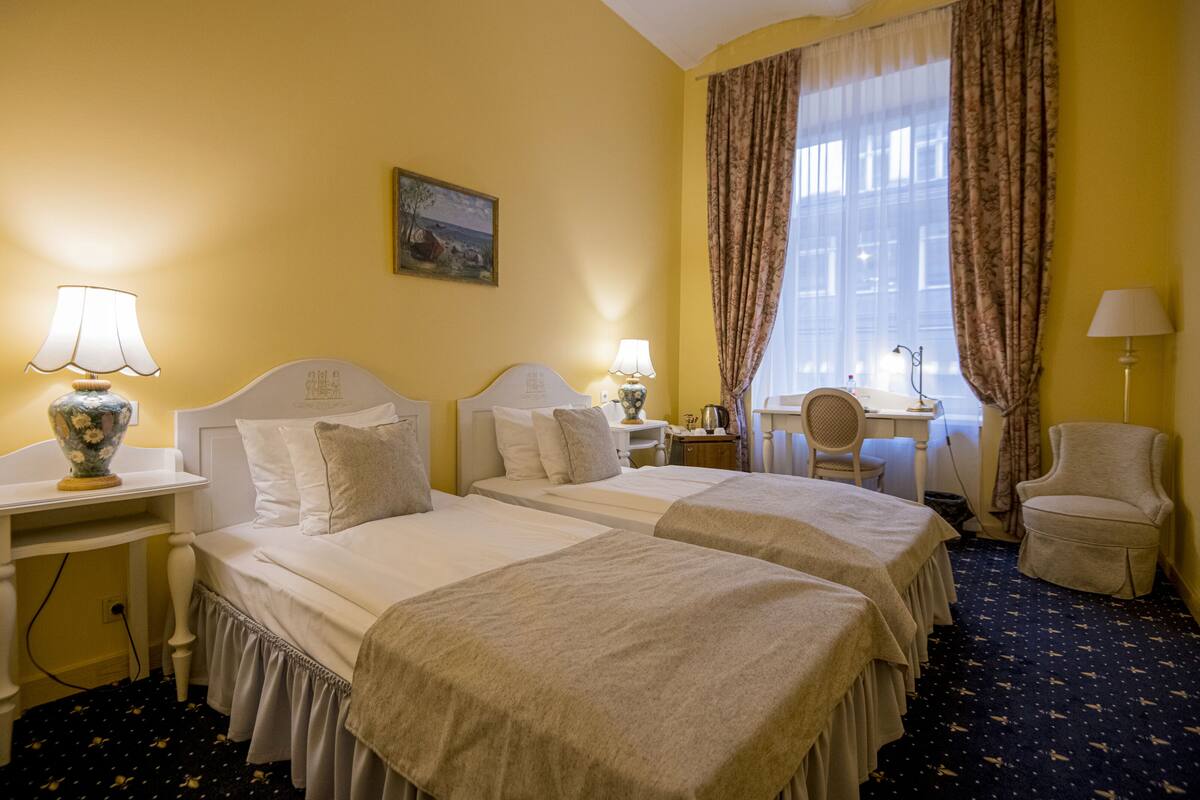 A hotel room with two beds, a desk, a chair, and a window with curtains.
