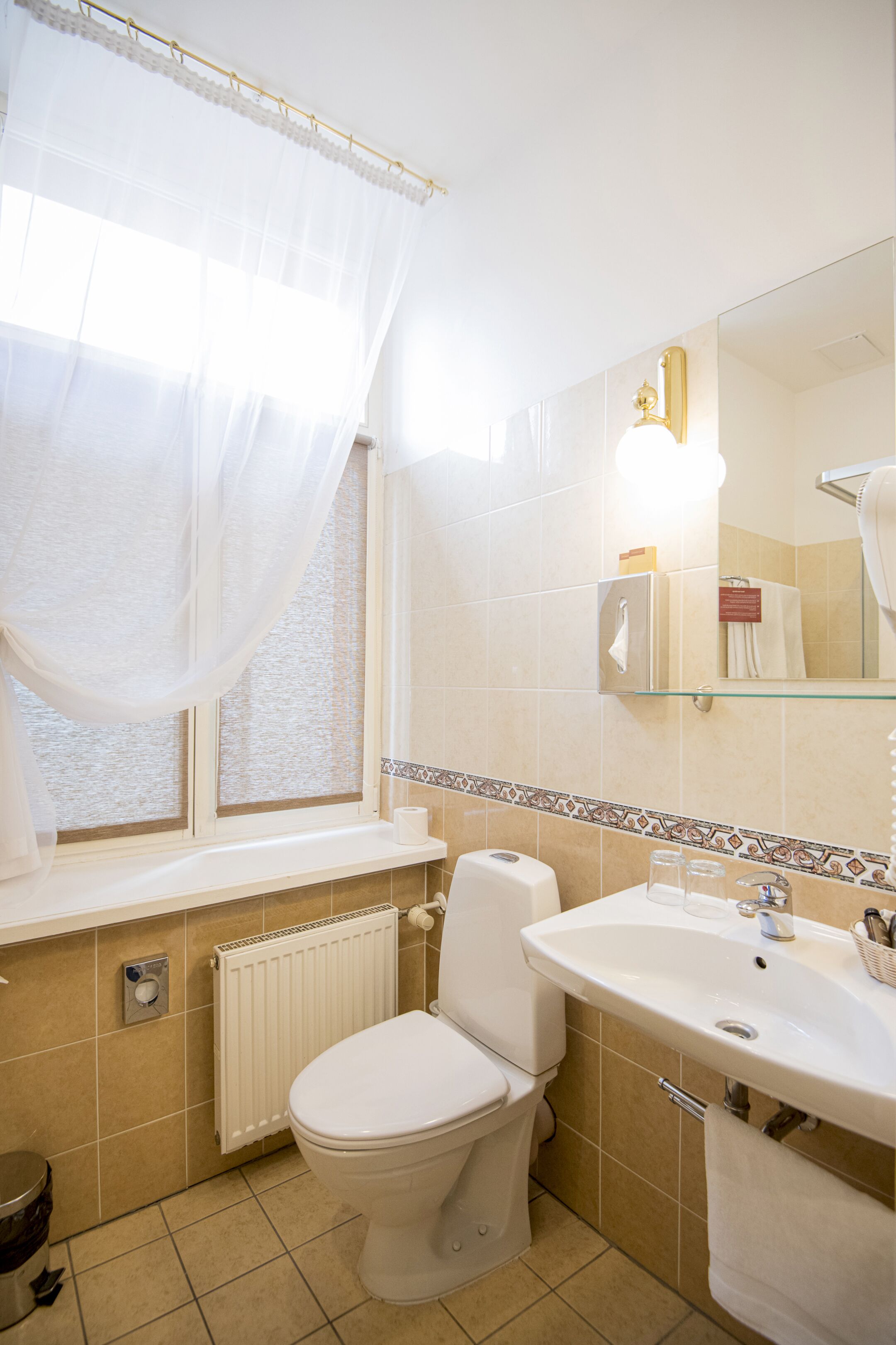 Un bagno con il water, un lavandino e una finestra con tende leggere.
