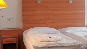 A hotel room with two beds, a wooden headboard, a bedside table with a lamp, and a power outlet. - Hotel Kaiser (Berlin)