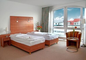 Habitación de hotel con dos camas, una mesita de noche, una silla y un ventanal con vistas.