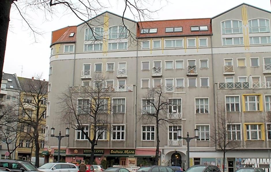 A multi-story building with a flat facade, several ground-level shops, and parked cars in front.
