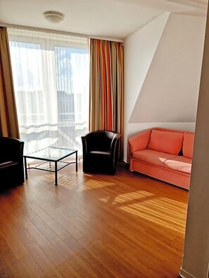 Una habitación con mesa de centro de vidrio, una silla negra, un sofá rojo y una ventana con cortinas.
