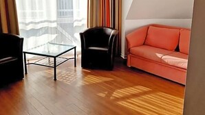 A room with a glass coffee table, a black chair, a red sofa, and a window with curtains. - Hotel Kaiser (Berlin)