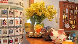 A counter with a display of travel brochures, a vase of yellow flowers, a piggy bank, and a wall with keys and a lock. - Hotel Kaiser (Berlin)