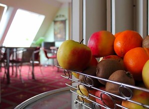 Una cesta de frutas con manzanas, naranjas y kiwis sobre un soporte de metal.