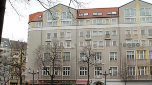 A multi-story building with a flat facade, several ground-level shops, and parked cars in front. - Hotel Kaiser (Berlin)