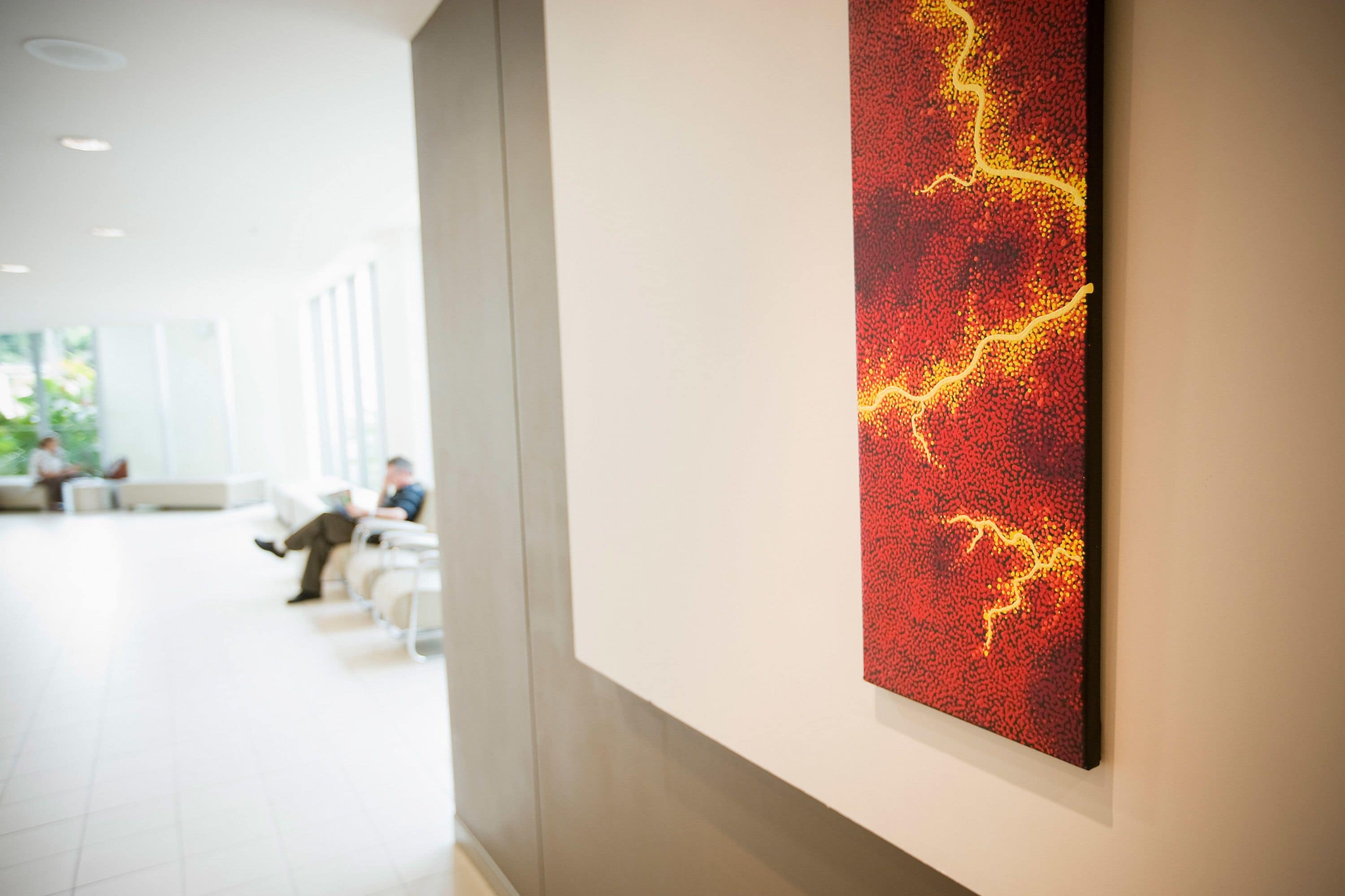 A modern interior with a red abstract painting on the wall, a seating area with white chairs, and a person in the background.