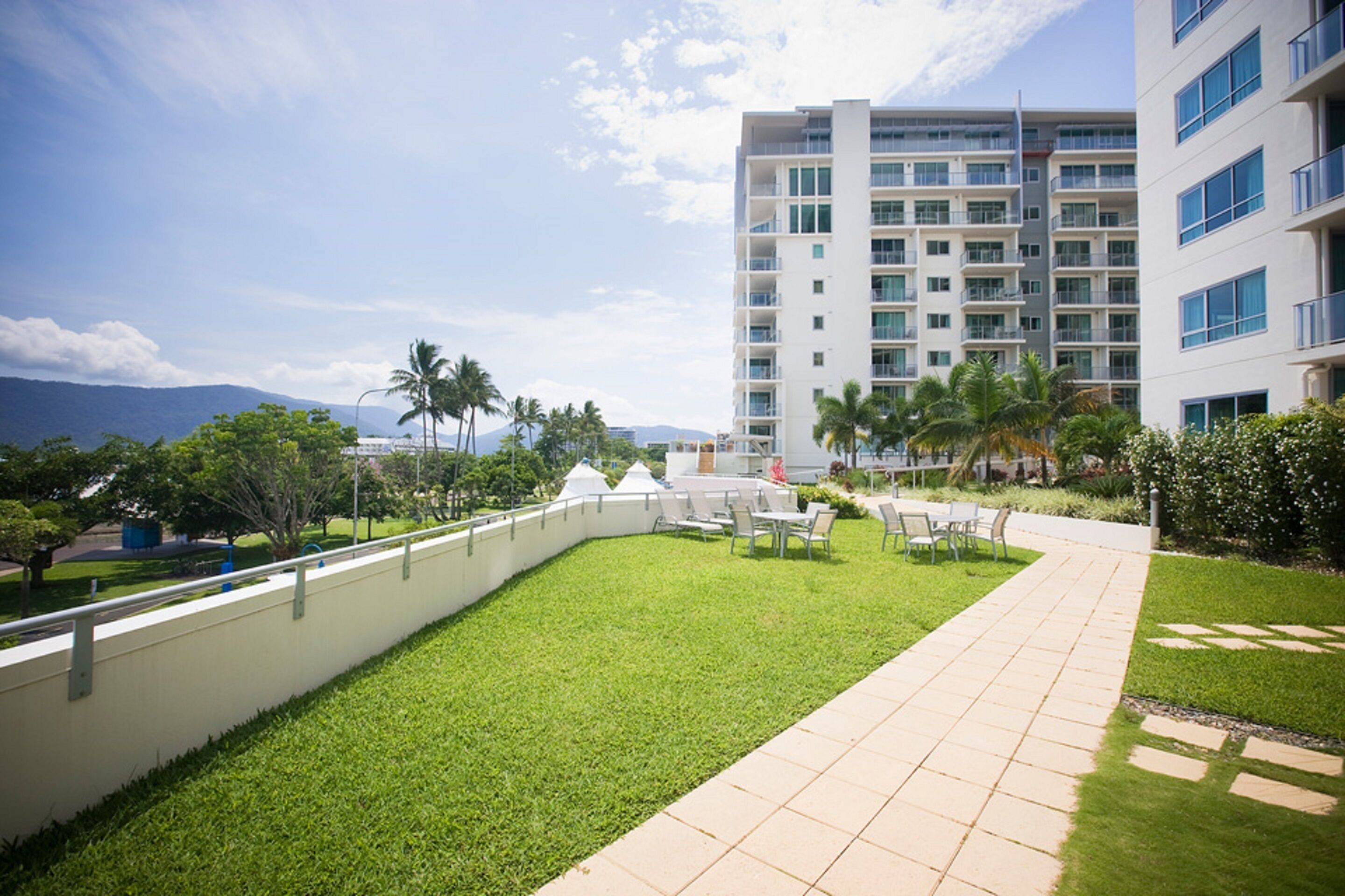 A hotel courtyard with a paved walkway, palm trees, and a view of a mountain range.