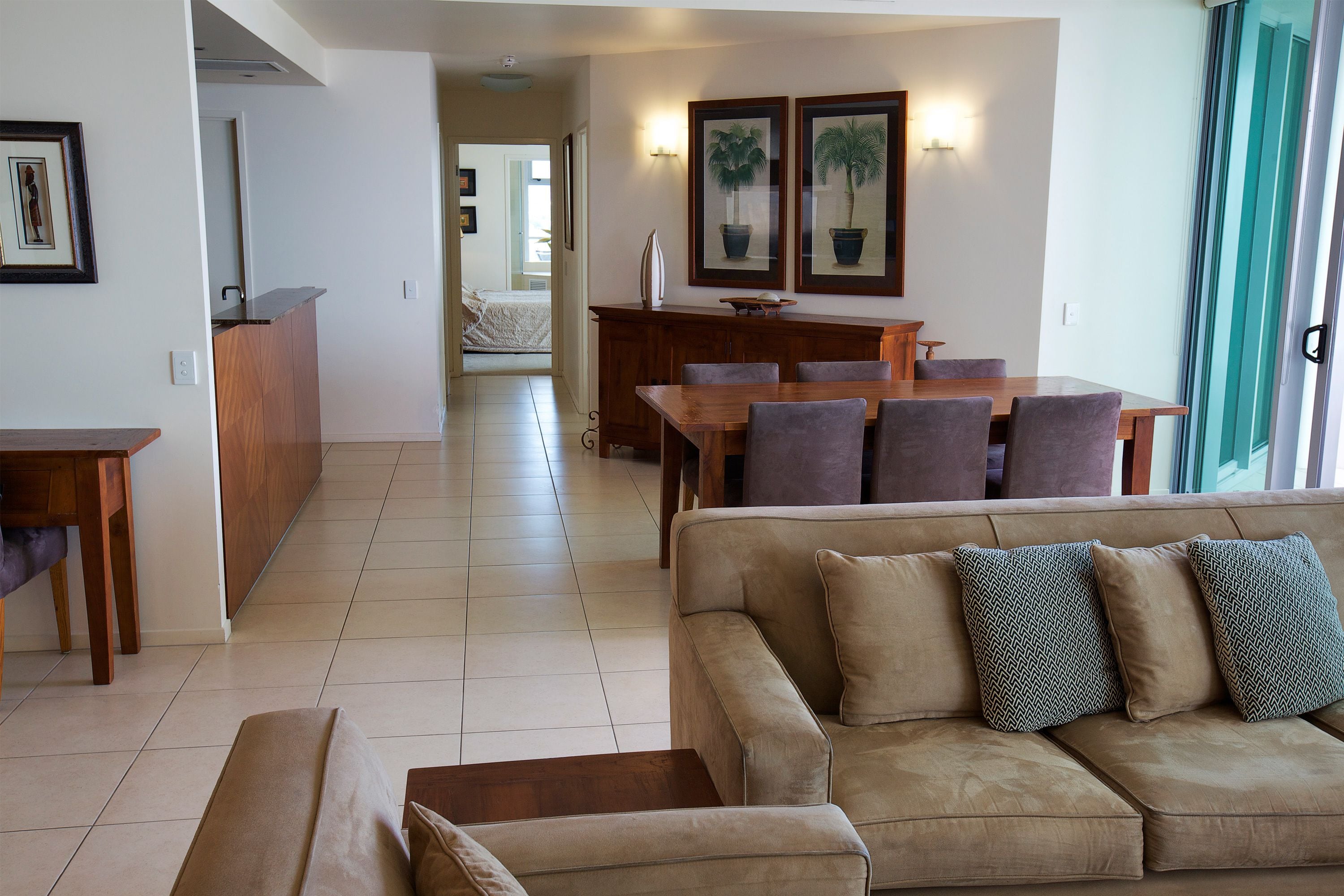 A spacious living area with a sofa, a dining table, and chairs. There is a kitchen area in the background.