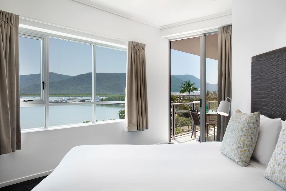 A hotel room with a bed, a desk, and a view of a body of water and mountains.