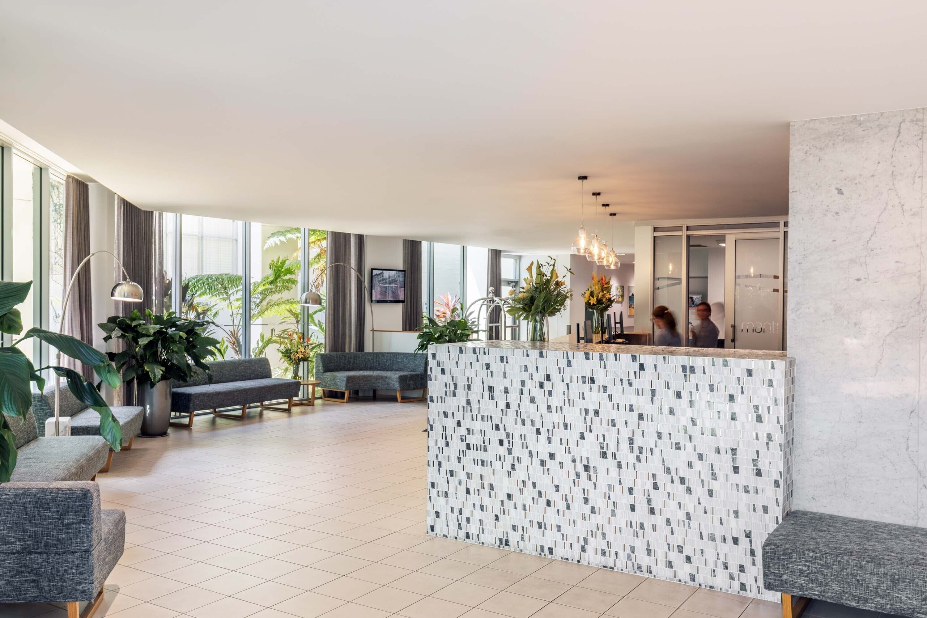 A modern lobby with a reception desk, seating area, and large windows.