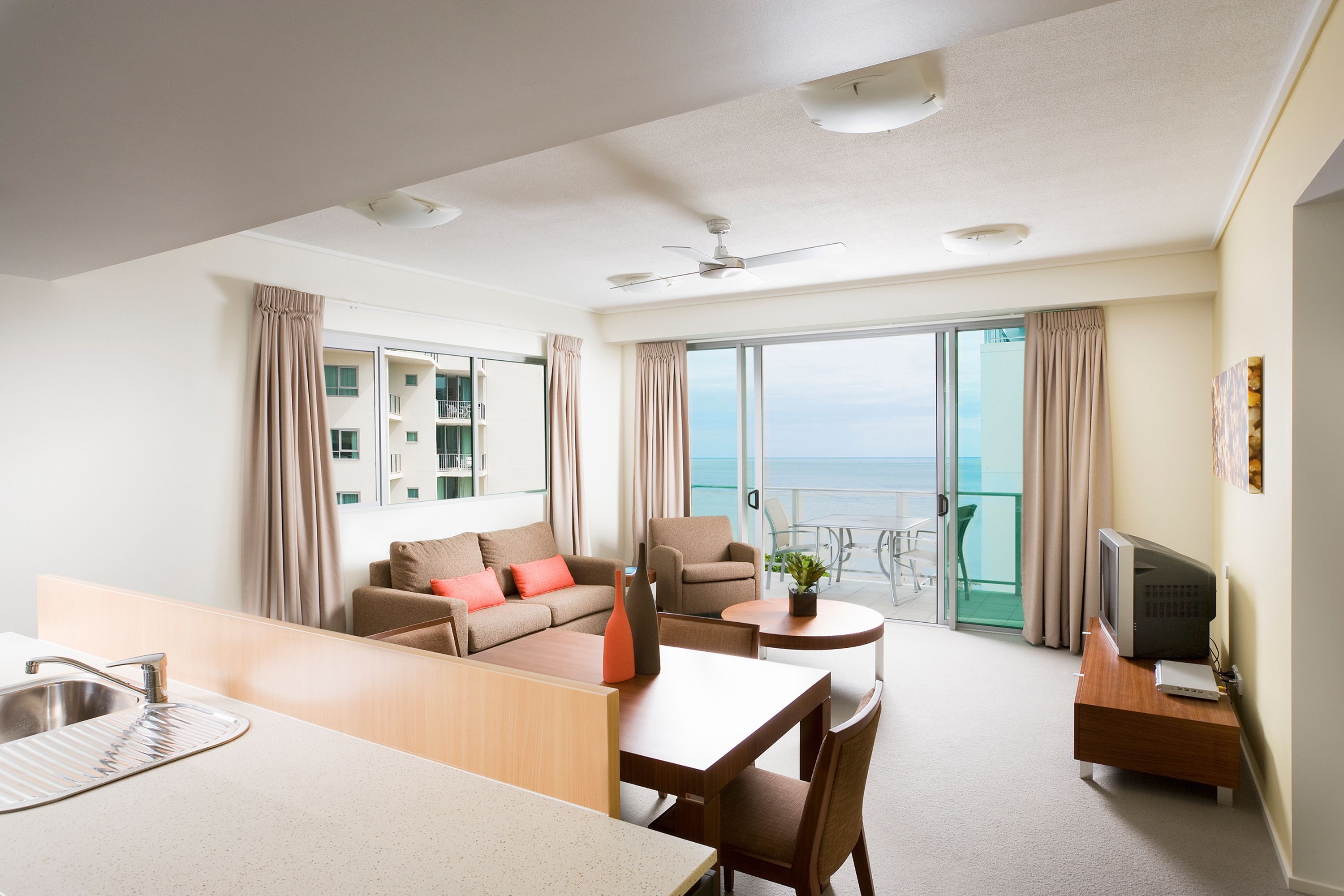 A modern hotel room with a balcony, a sofa, a dining table, and a TV.
