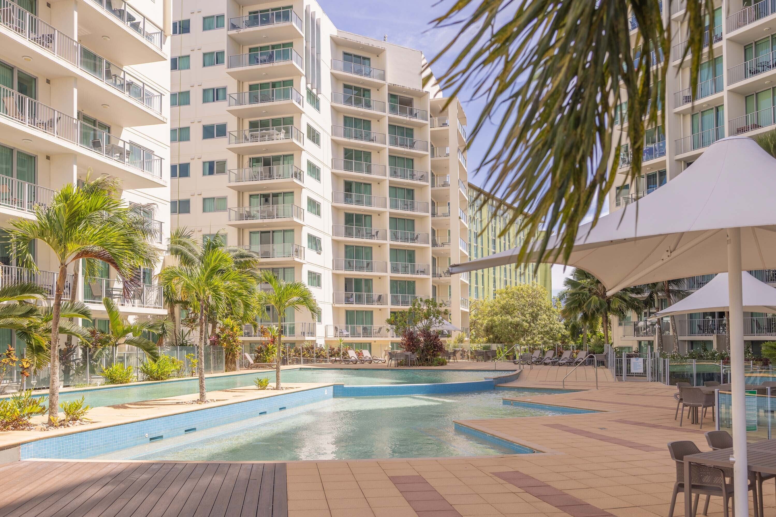 A hotel with multiple balconies, a swimming pool, and outdoor seating areas.