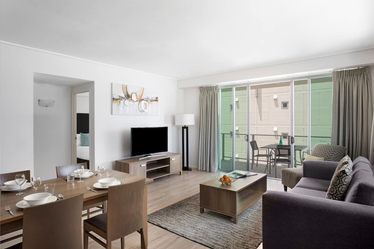 A modern living room with a dining area, a flat-screen TV, and a balcony with a table and chairs.