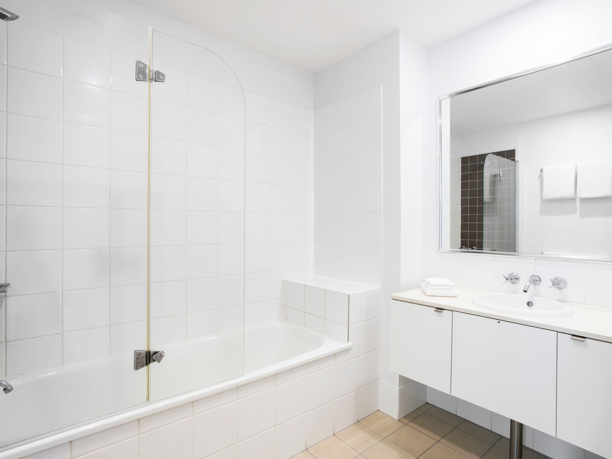 Un baño moderno con baldosas blancas, ducha con mampara de cristal, bañera independiente y tocador con espejo.