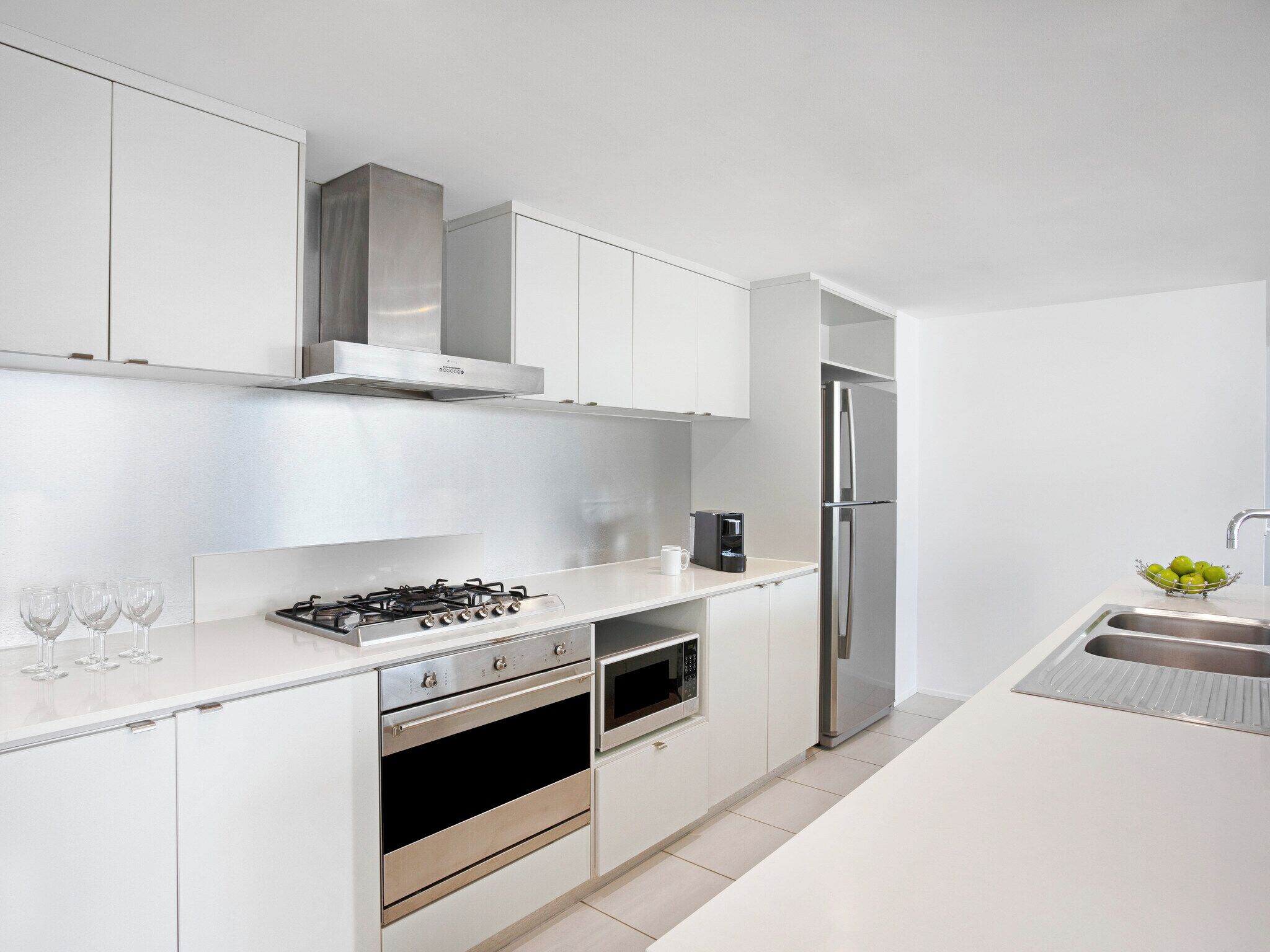 A modern kitchen with white cabinetry, stainless steel appliances, and a built-in oven.