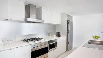 A modern kitchen with white cabinetry, stainless steel appliances, and a built-in oven.