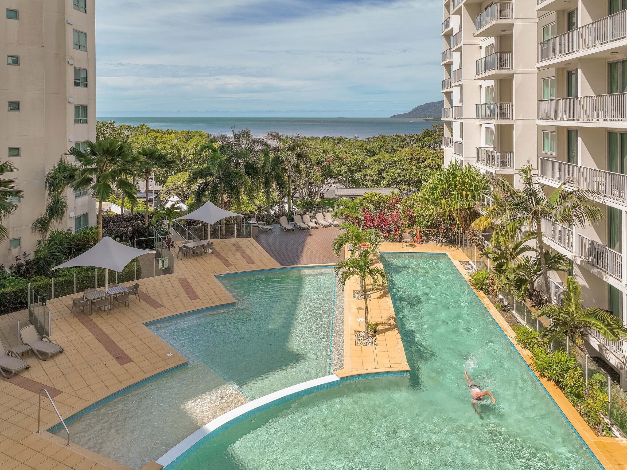 A pool area with clear water, lounge chairs, and a view of the ocean.