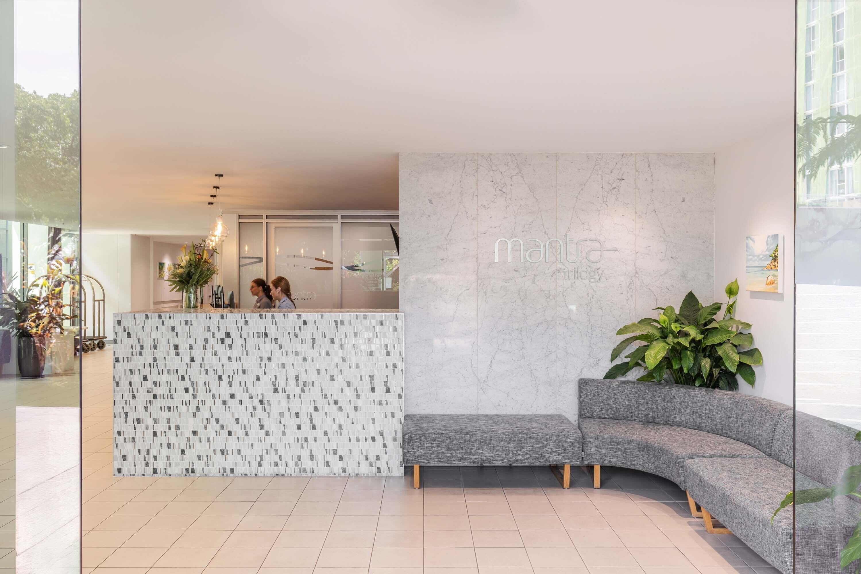 A modern reception area with a marble wall, a patterned reception desk, and a grey sofa.