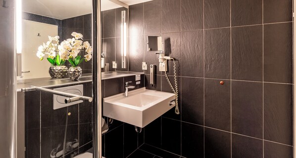 A modern bathroom with a glass shower enclosure, a white sink, and a mirror.