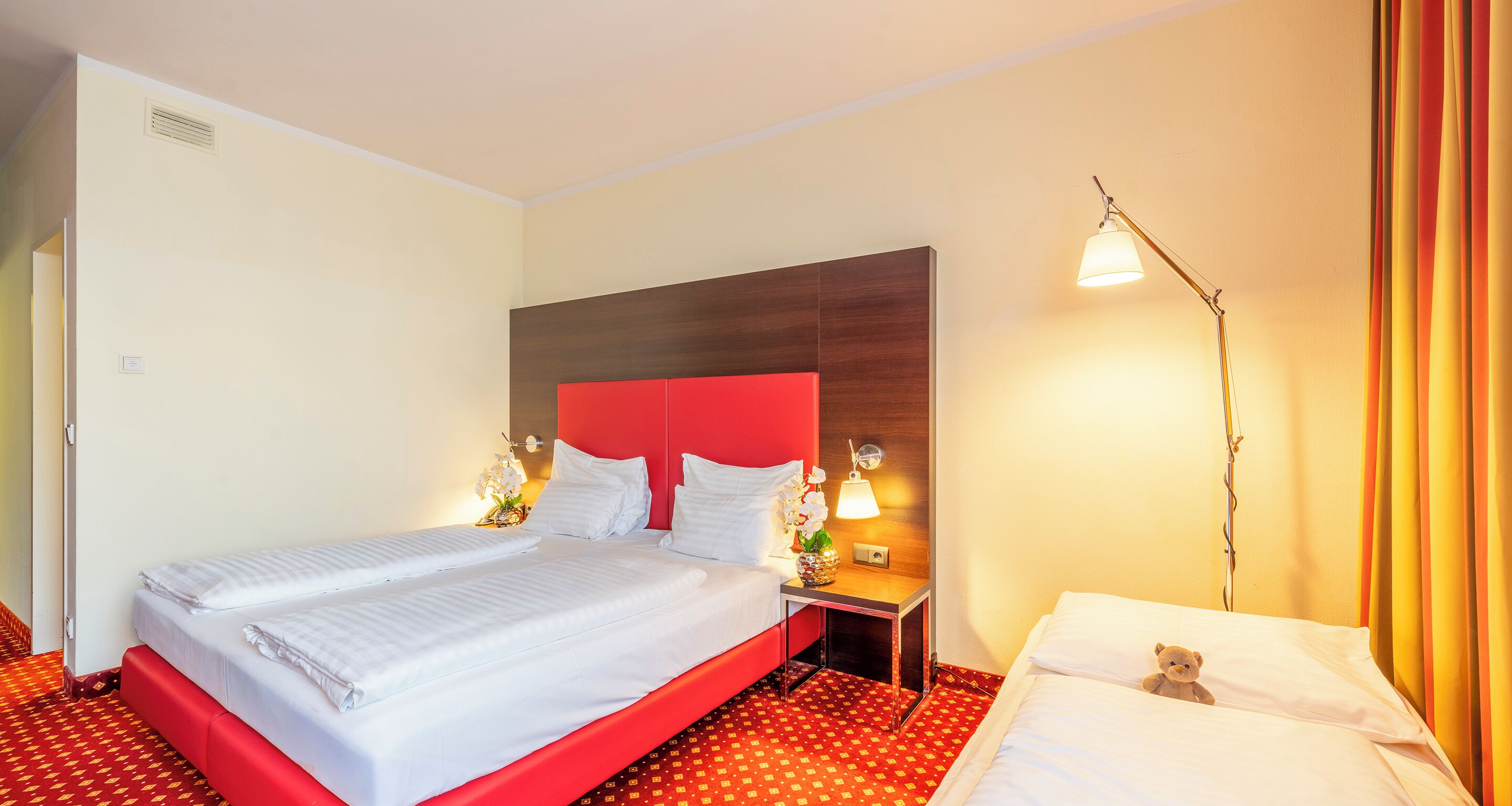 Una camera d'albergo con un letto grande, un comodino con una lampada e un altro comodino con un vaso di fiori.