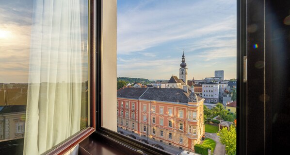 A view from a window overlooking a historic building with a clock tower, surrounded by other buildings and greenery.