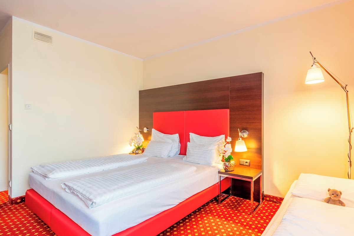 Habitación de hotel con cama, mesita de noche, l ámpara y un oso de peluche sobre la cama.