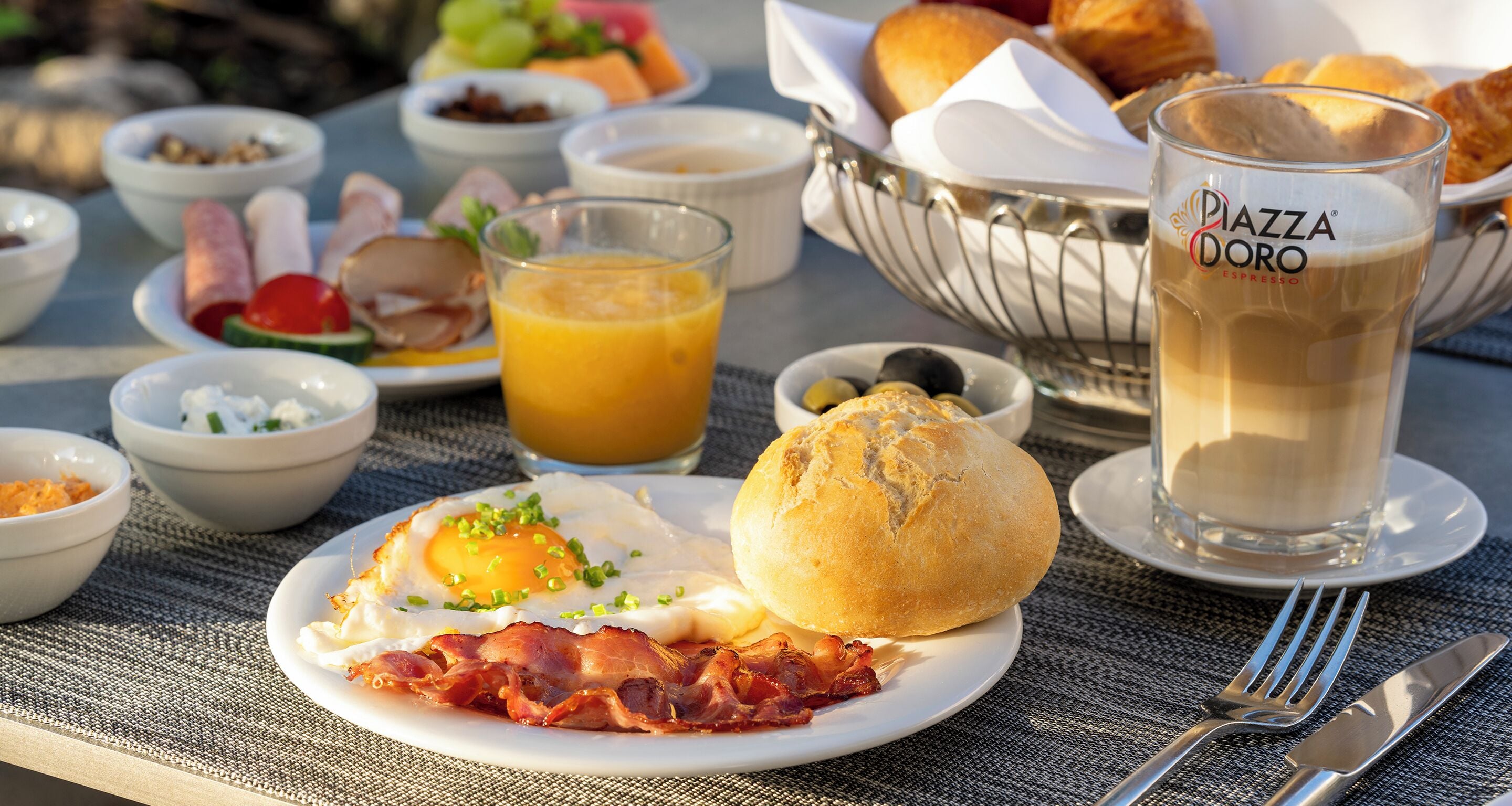 Desayuno con un plato de huevos, tocino y tostadas, un vaso de jugo de naranja y un café espresso.