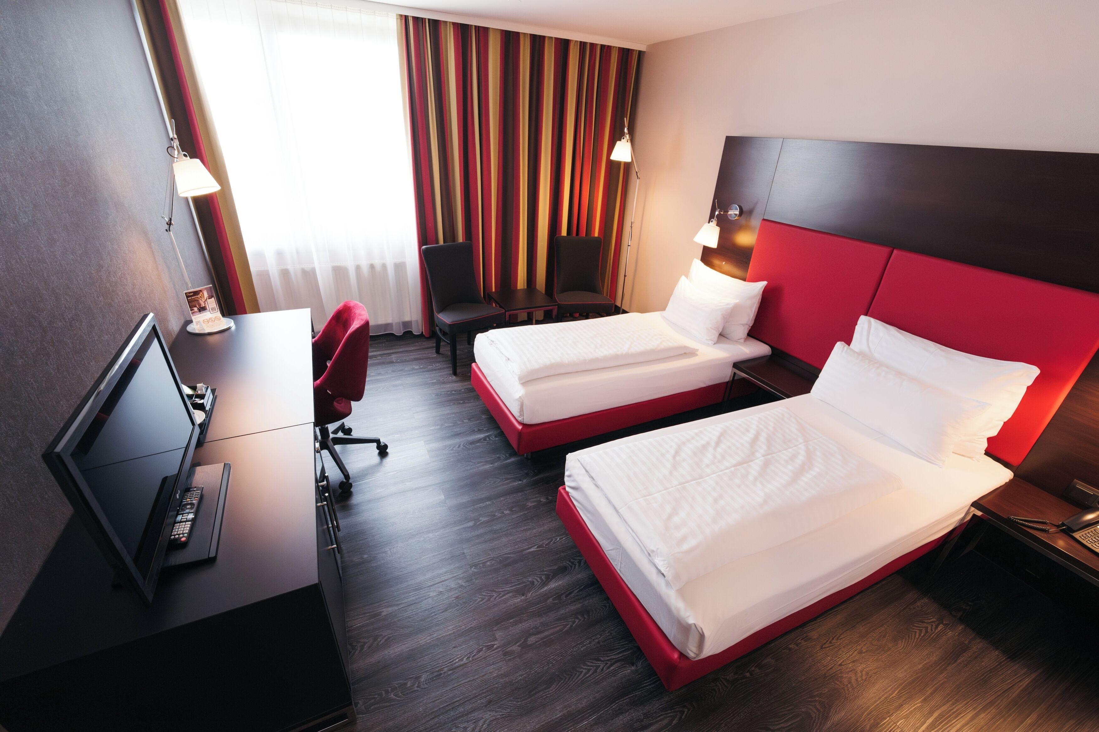 A hotel room with two beds, a desk with a computer, a chair, and a TV.