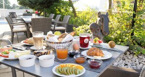 An outdoor dining table with breakfast items including croissants, fruit, and beverages.