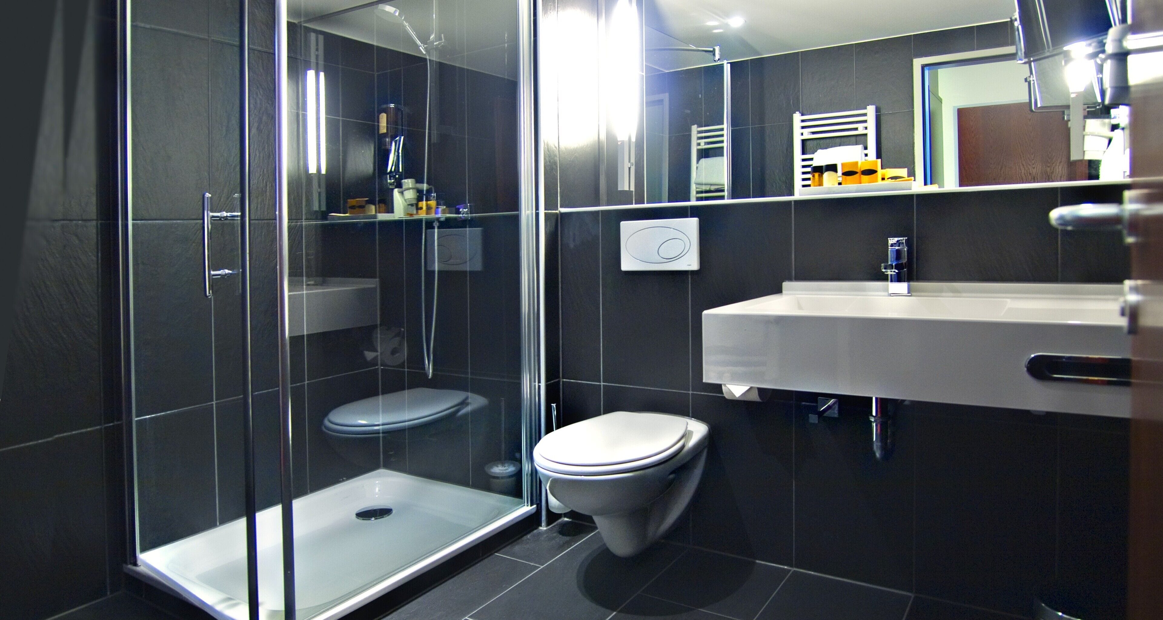 A modern bathroom with a glass-enclosed shower, a white toilet, and a white sink with a mirror above it.