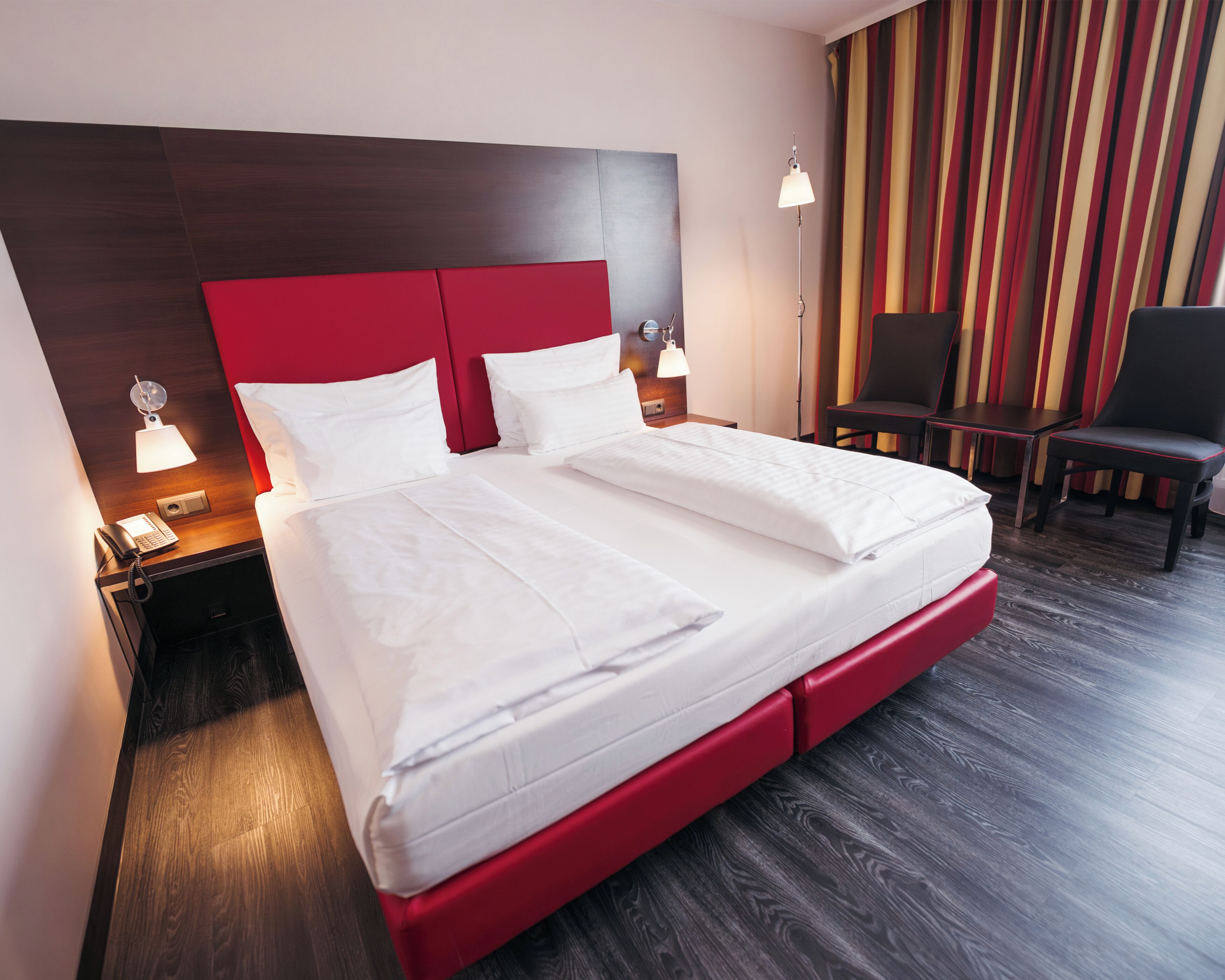 A hotel room with a large bed, bedside lamps, a desk with a telephone, and a chair.