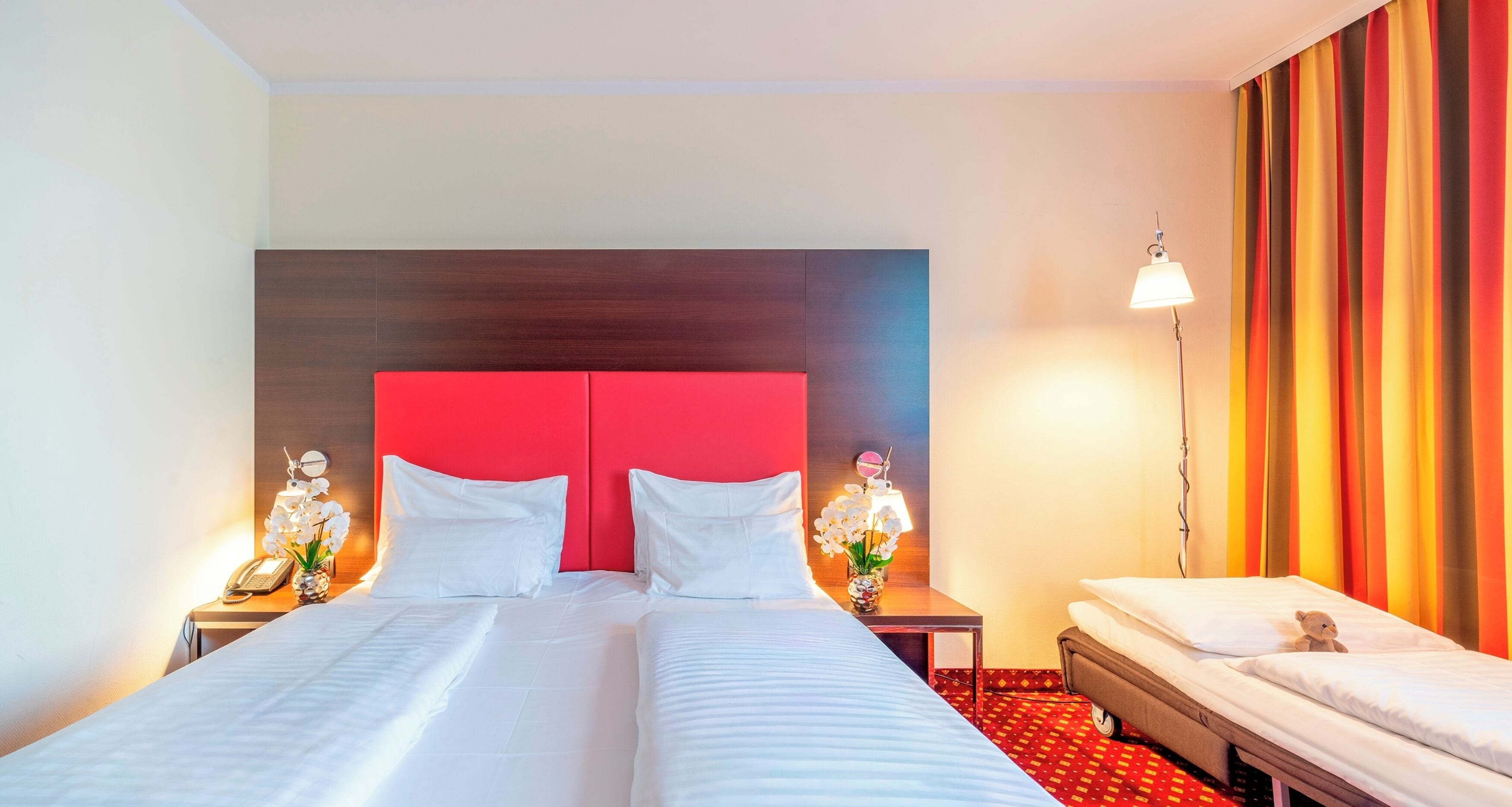 A hotel room with a large bed, a bedside table with a lamp, a small table with a vase of flowers, and a sofa bed.