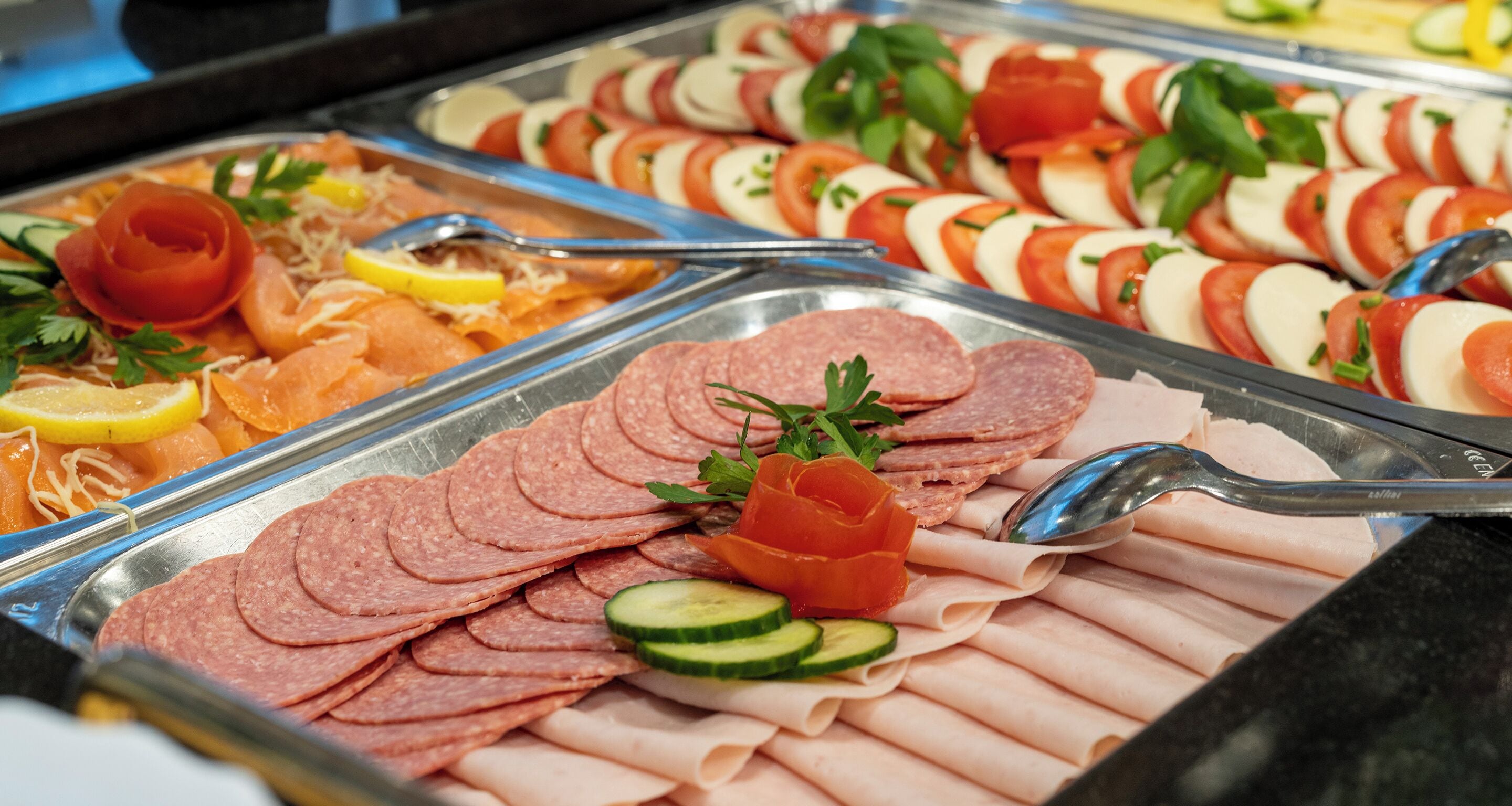 A buffet with various meats, including sliced salami, ham, and smoked salmon, garnished with herbs and lemon slices.