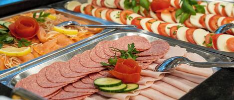 A buffet with various meats, including sliced salami, ham, and smoked salmon, garnished with herbs and lemon slices.