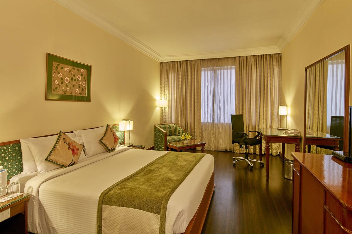Une chambre d’hôtel avec un grand lit, un bureau avec une chaise, une télévision et une fenêtre avec des rideaux.