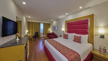 Habitación de hotel con una cama grande, un escritorio, un televisor de pantalla plana, una silla, una mesita y vistas a la ciudad.
